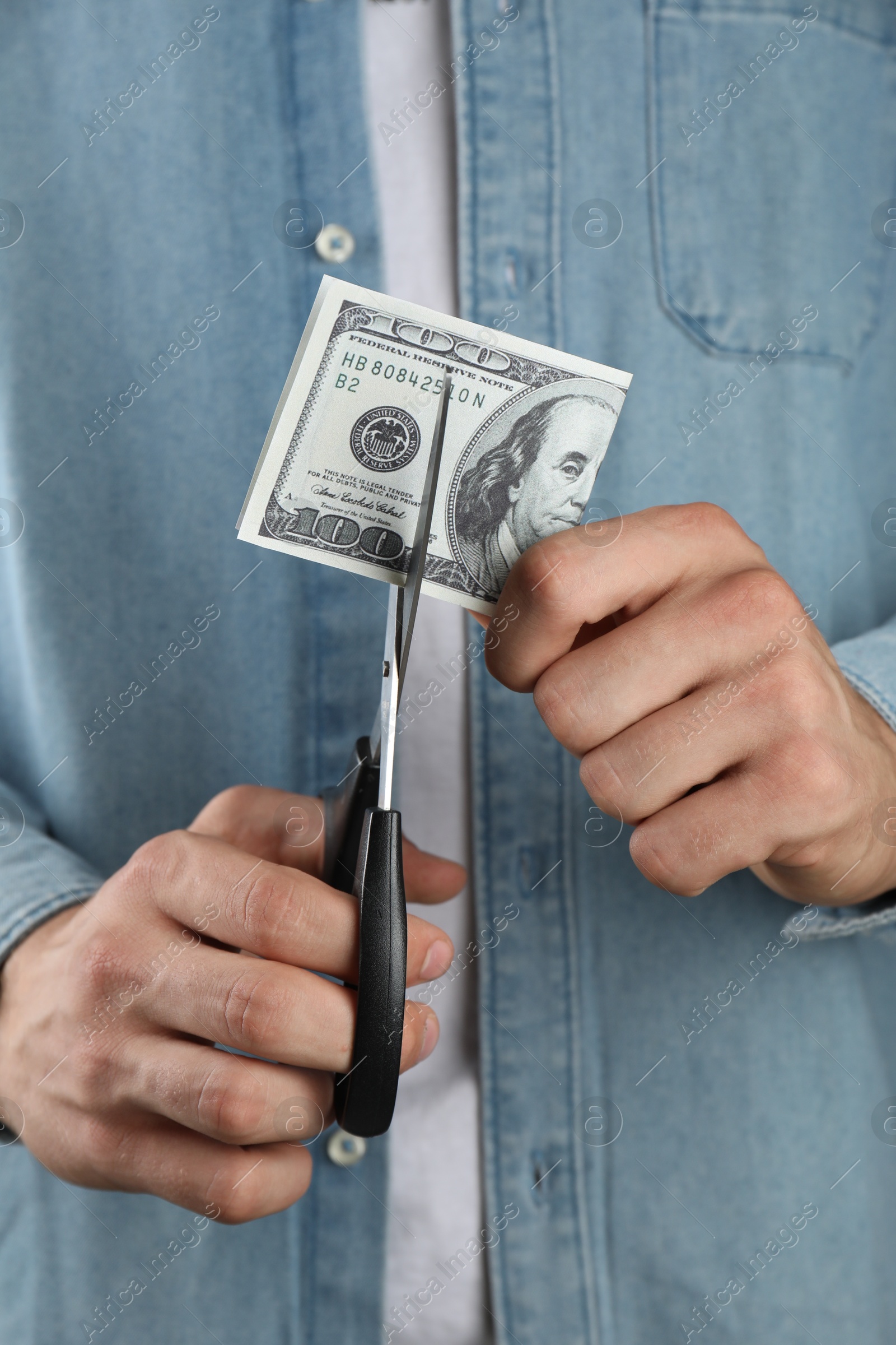 Photo of Budgeting. Man cutting dollar banknote with scissors, closeup