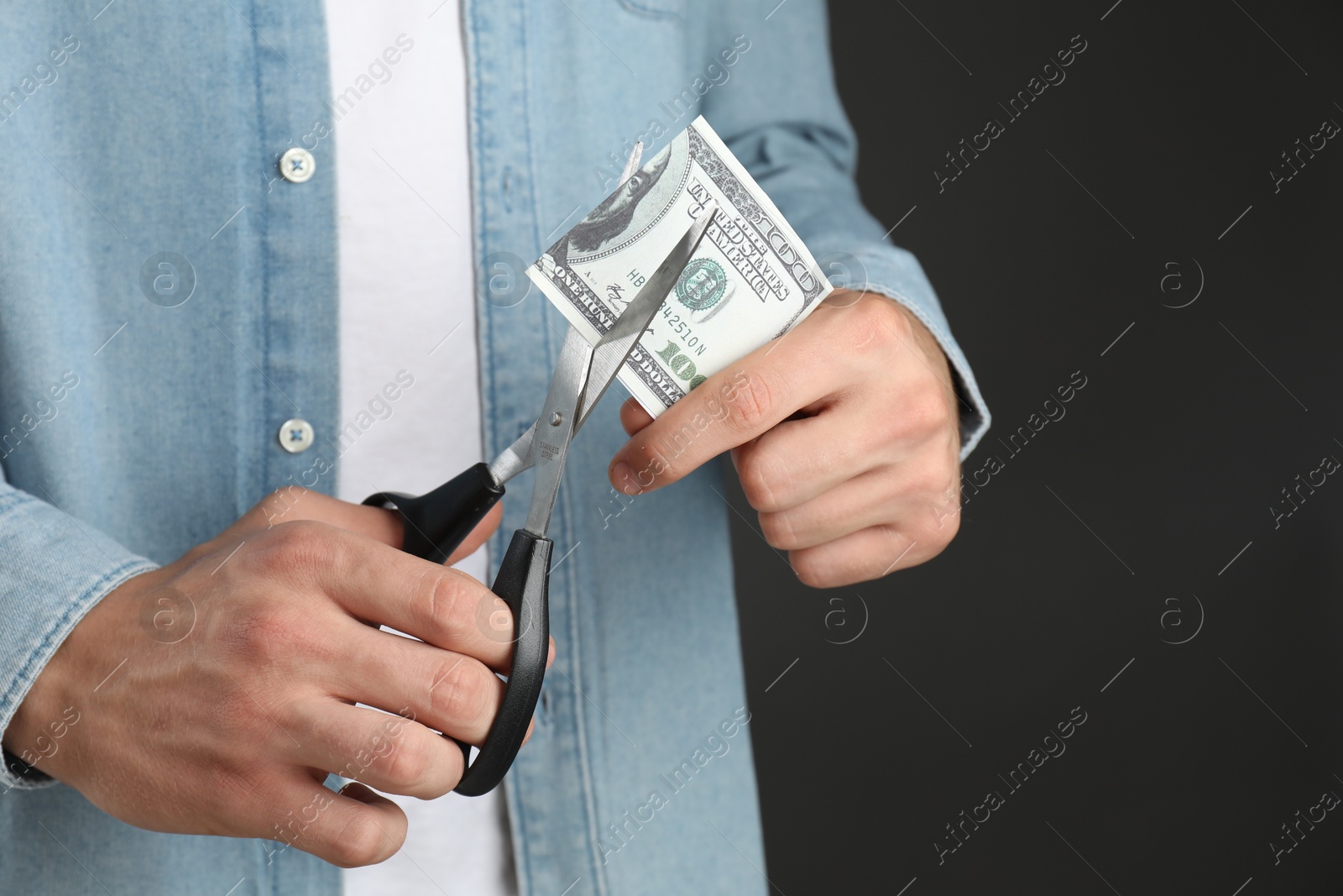 Photo of Budgeting. Man cutting dollar banknote with scissors on dark grey background, closeup. Space for text