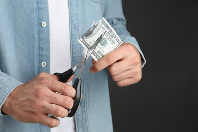 Photo of Budgeting. Man cutting dollar banknote with scissors on dark grey background, closeup. Space for text