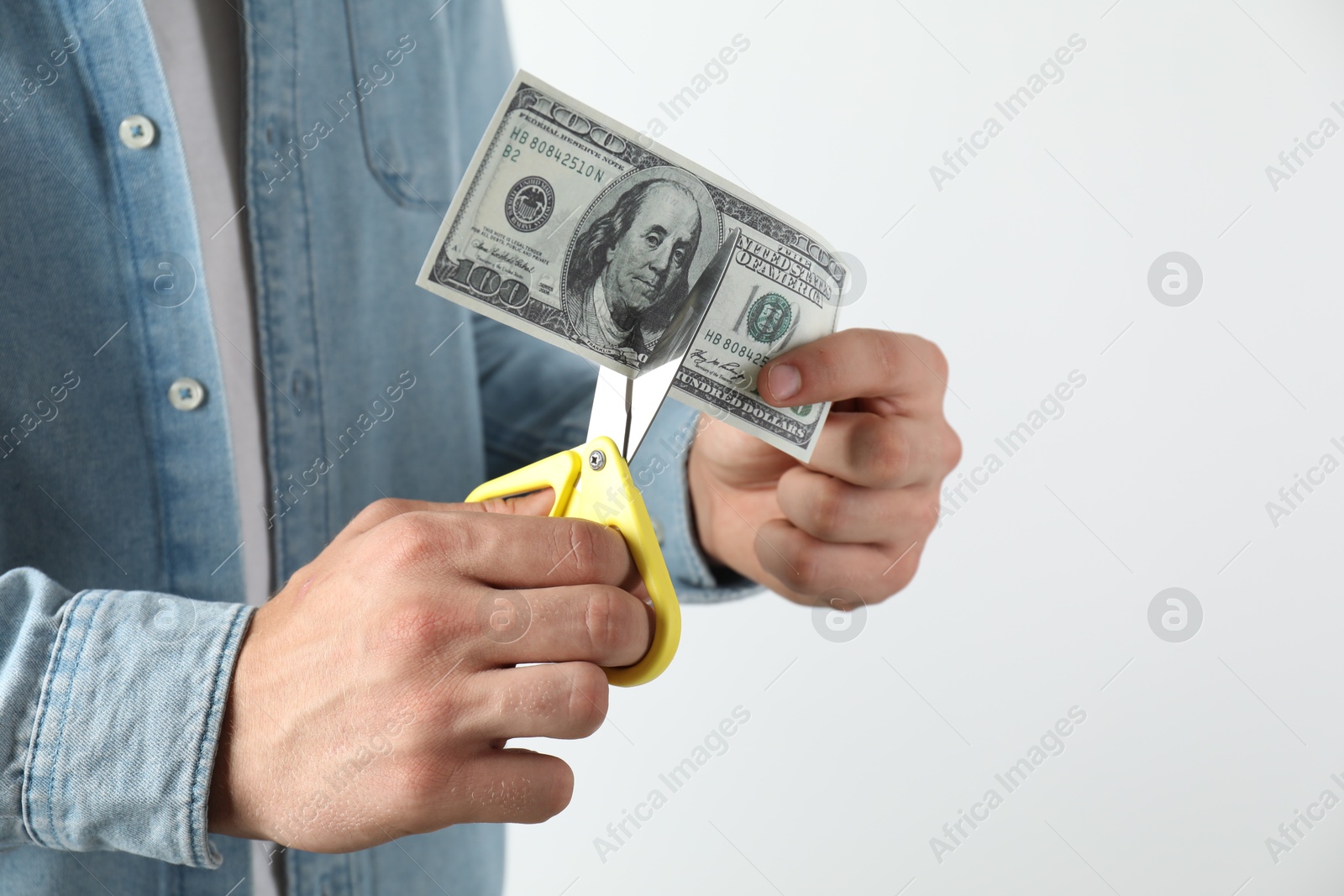 Photo of Budgeting. Man cutting dollar banknote with scissors on light grey background, closeup. Space for text