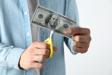 Photo of Budgeting. Man cutting dollar banknote with scissors on light grey background, closeup