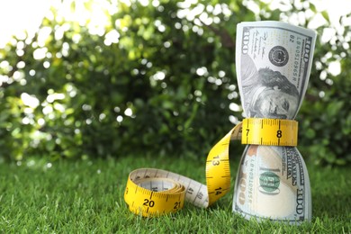 Photo of Budgeting. Dollar banknotes and measuring tape on green grass, space for text