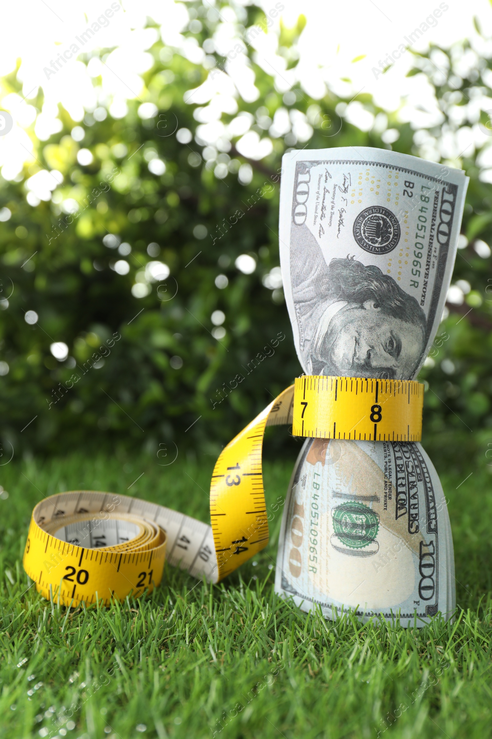 Photo of Budgeting. Dollar banknotes and measuring tape on green grass