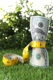 Photo of Budgeting. Dollar banknotes and measuring tape on green grass