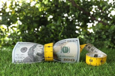 Photo of Budgeting. Dollar banknotes and measuring tape on green grass