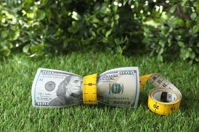 Photo of Budgeting. Dollar banknotes and measuring tape on green grass