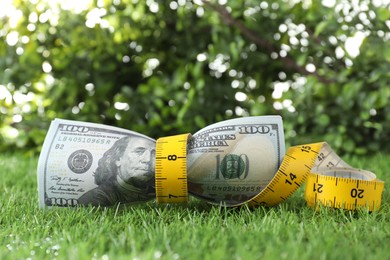 Photo of Budgeting. Dollar banknotes and measuring tape on green grass