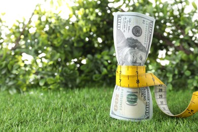 Photo of Budgeting. Dollar banknotes and measuring tape on green grass, space for text