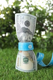 Photo of Budgeting. Dollar banknotes and measuring tape on green grass