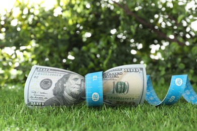 Photo of Budgeting. Dollar banknotes and measuring tape on green grass