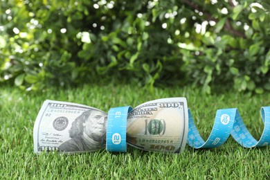 Photo of Budgeting. Dollar banknotes and measuring tape on green grass