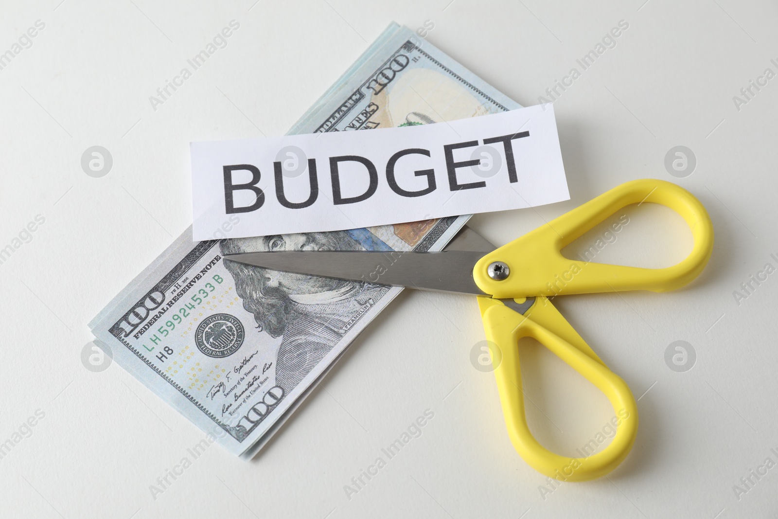 Photo of Dollar banknotes, scissors and paper with word Budget on white background