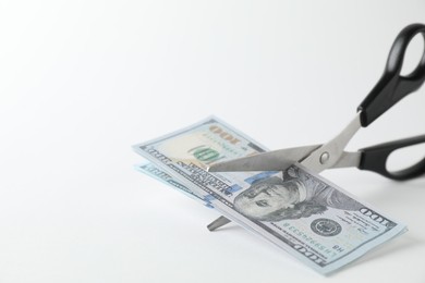 Photo of Budgeting. Cutting dollar banknotes with scissors on white background, closeup. Space for text