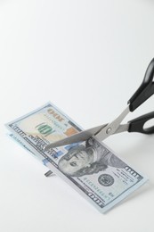 Photo of Budgeting. Cutting dollar banknotes with scissors on white background, closeup