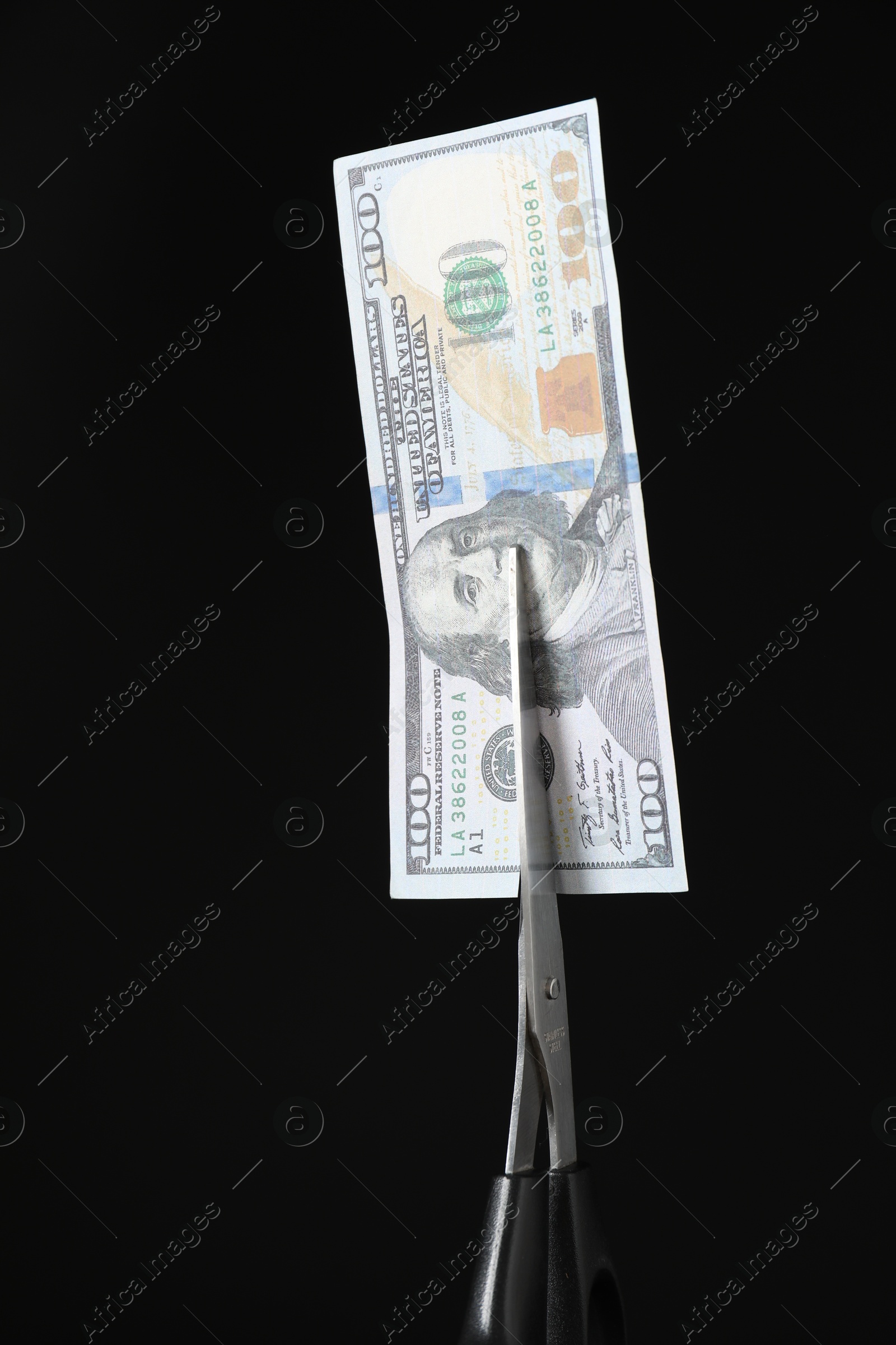 Photo of Budgeting. Cutting dollar banknote with scissors on black background, closeup