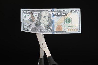 Photo of Budgeting. Cutting dollar banknote with scissors on black background, closeup