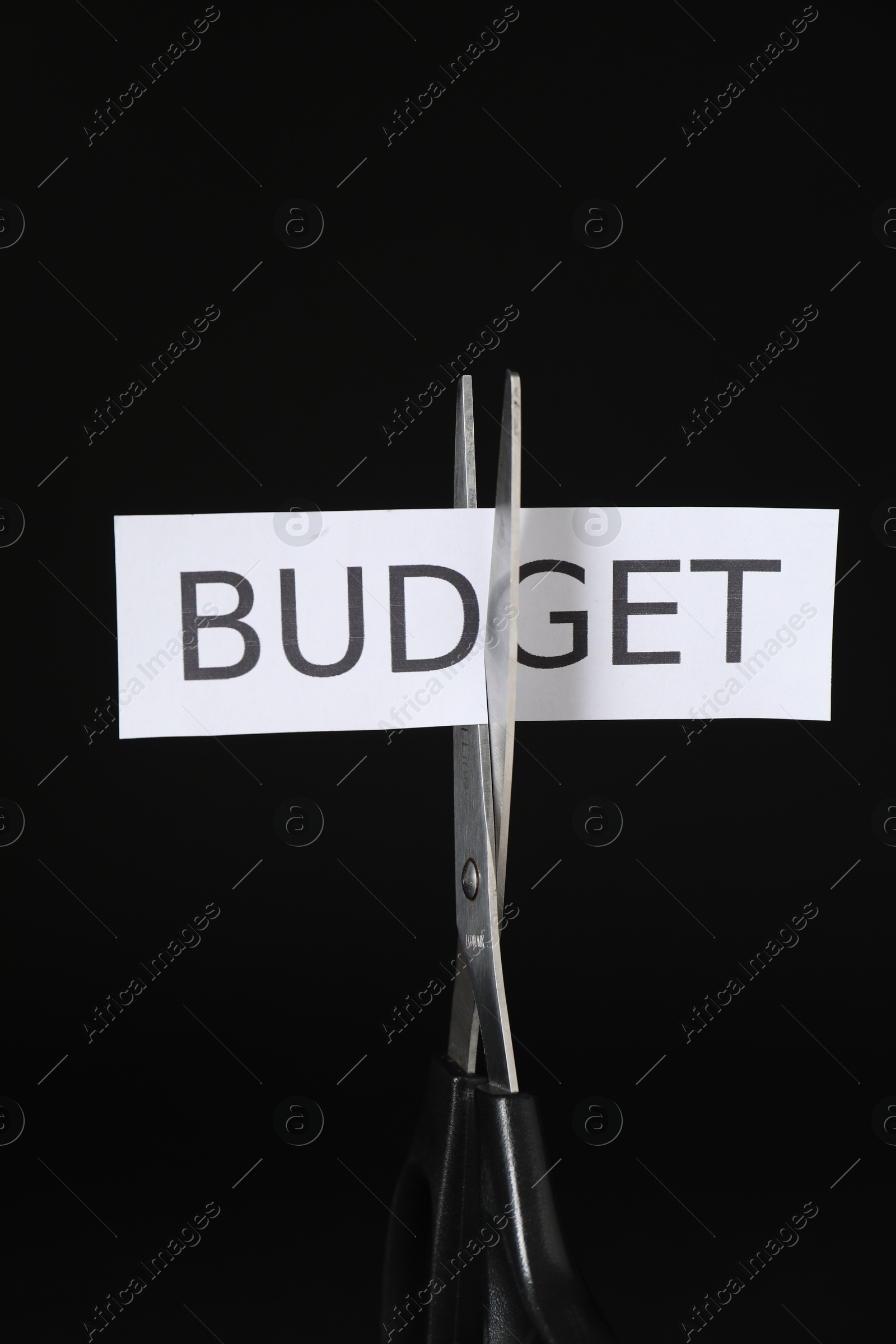 Photo of Cutting paper with word Budget with scissors on black background, closeup