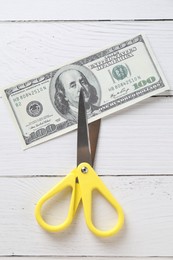 Photo of Budgeting. Dollar banknote with scissors on white wooden table, top view