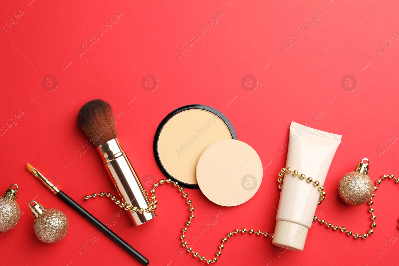 Photo of Flat lay composition with makeup products and Christmas decor on red background. Space for text