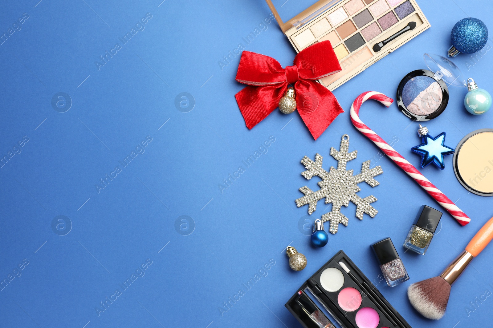 Photo of Flat lay composition with makeup products and Christmas decor on blue background. Space for text