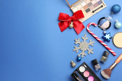 Flat lay composition with makeup products and Christmas decor on blue background. Space for text