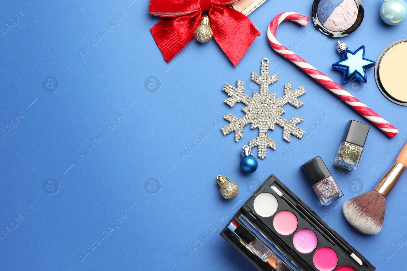 Photo of Flat lay composition with makeup products and Christmas decor on blue background. Space for text