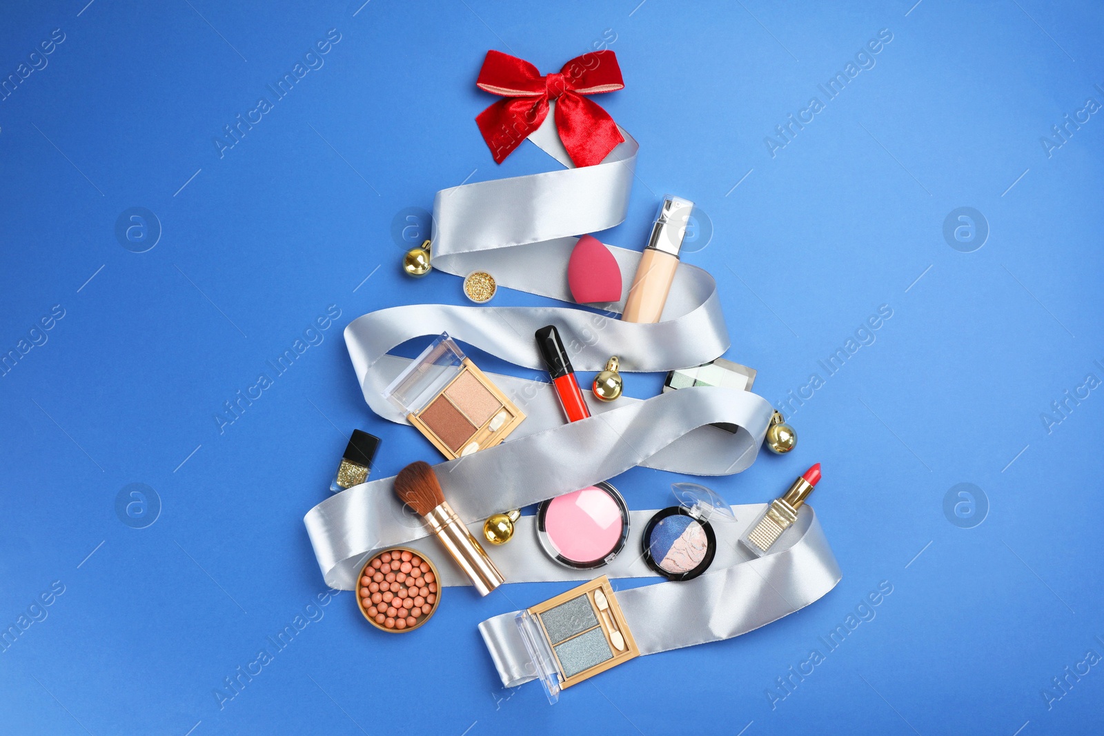 Photo of Christmas tree made of decorative cosmetic products and festive decor on blue background