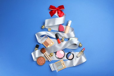 Photo of Christmas tree made of decorative cosmetic products and festive decor on blue background