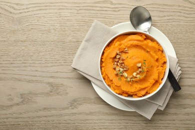 Delicious mashed sweet potatoes in bowl and spoon on wooden table, top view. Space for text