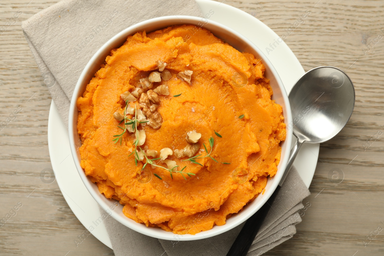 Photo of Delicious mashed sweet potatoes in bowl and spoon on wooden table, top view