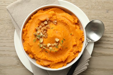 Delicious mashed sweet potatoes in bowl and spoon on wooden table, top view