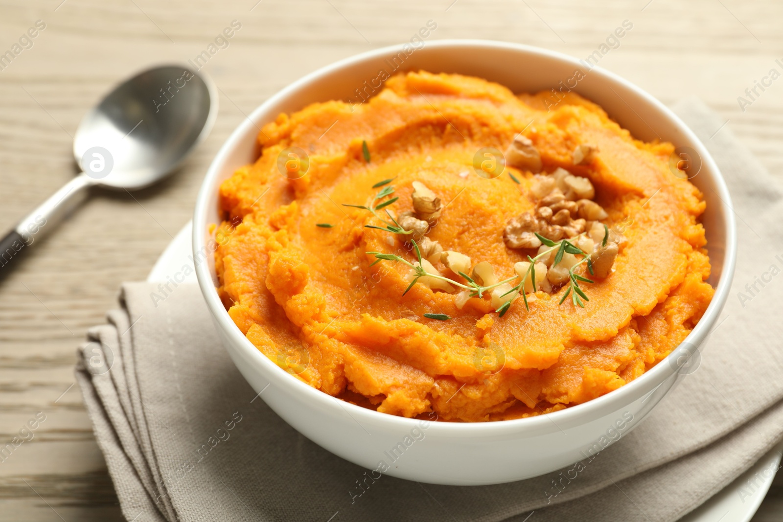 Photo of Delicious mashed sweet potatoes in bowl and spoon on wooden table, closeup