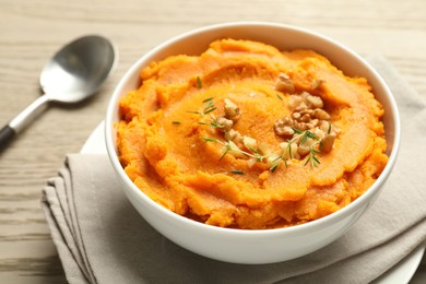 Delicious mashed sweet potatoes in bowl and spoon on wooden table, closeup