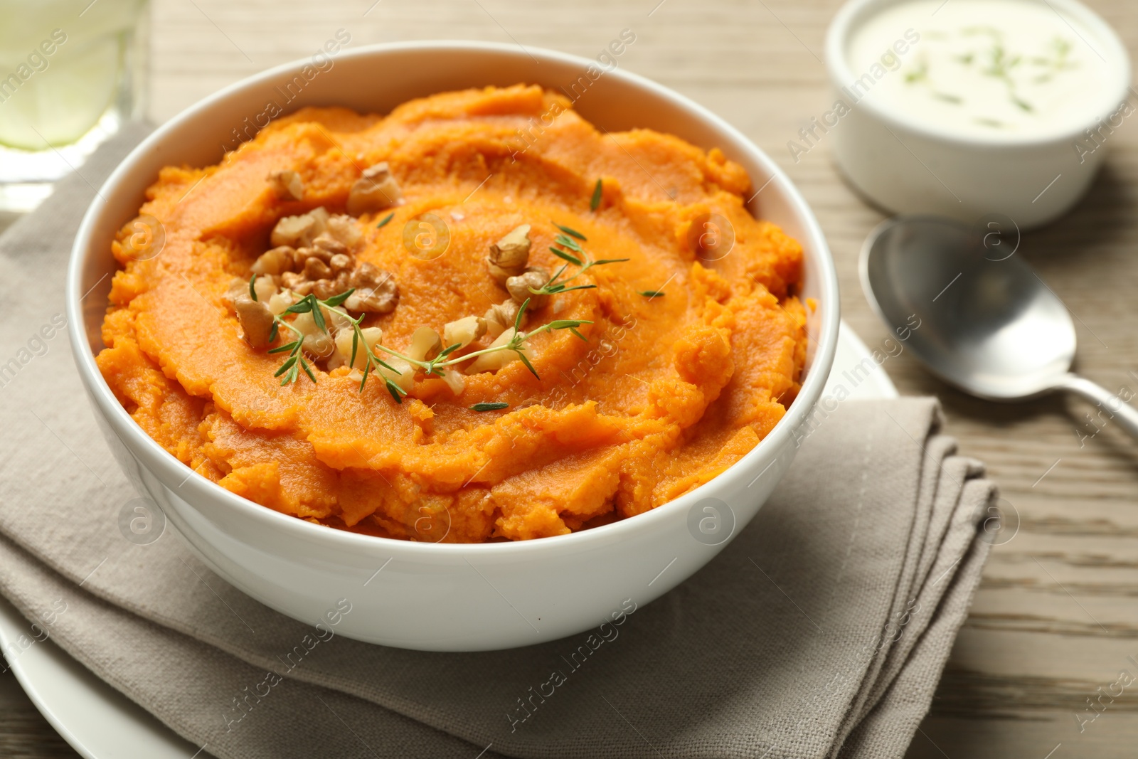 Photo of Delicious mashed sweet potatoes in bowl and spoon on wooden table, closeup