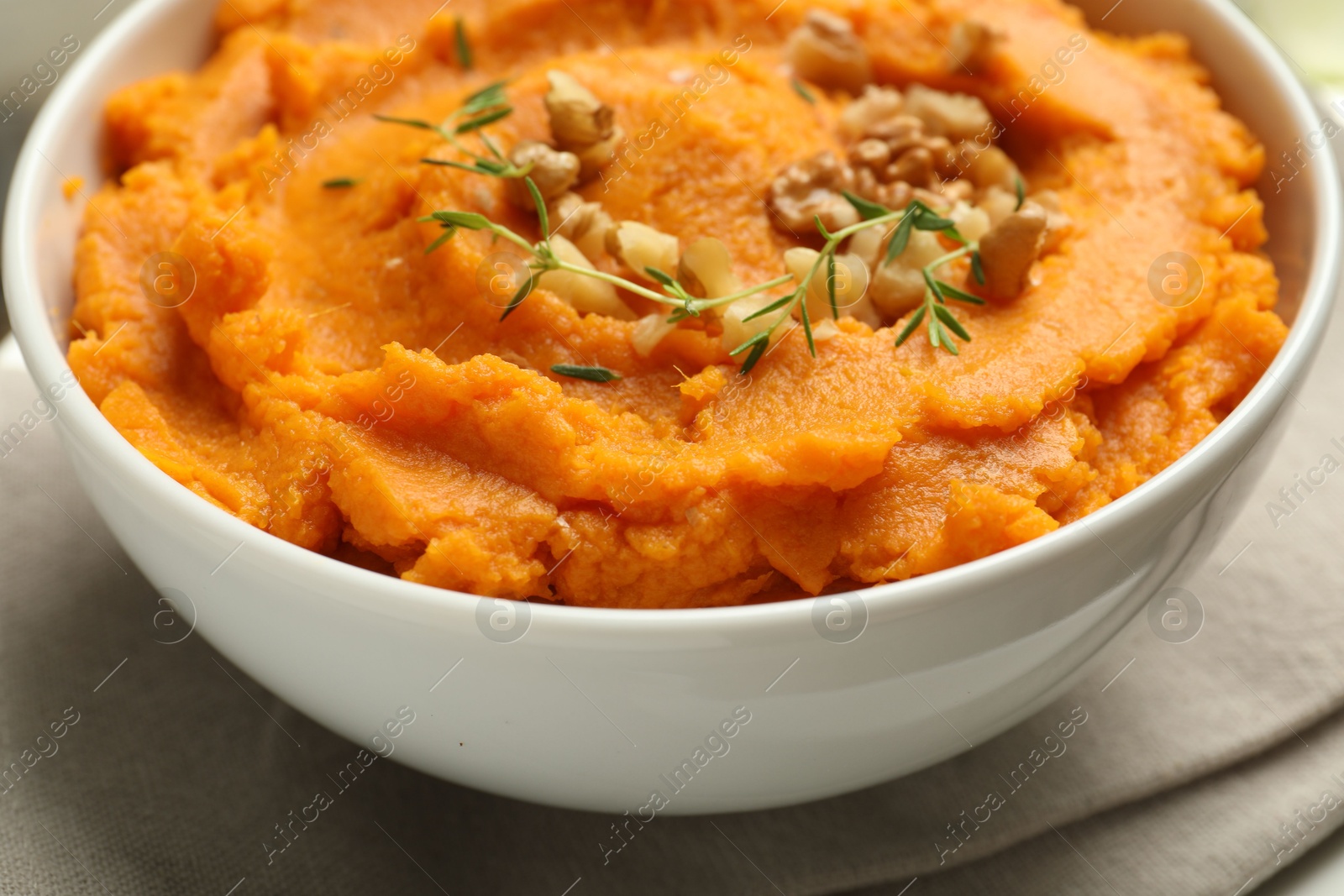 Photo of Delicious mashed sweet potatoes and nuts in bowl on table, closeup