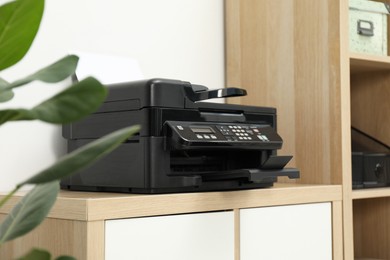 Photo of Modern printer with paper on wooden nightstand in office