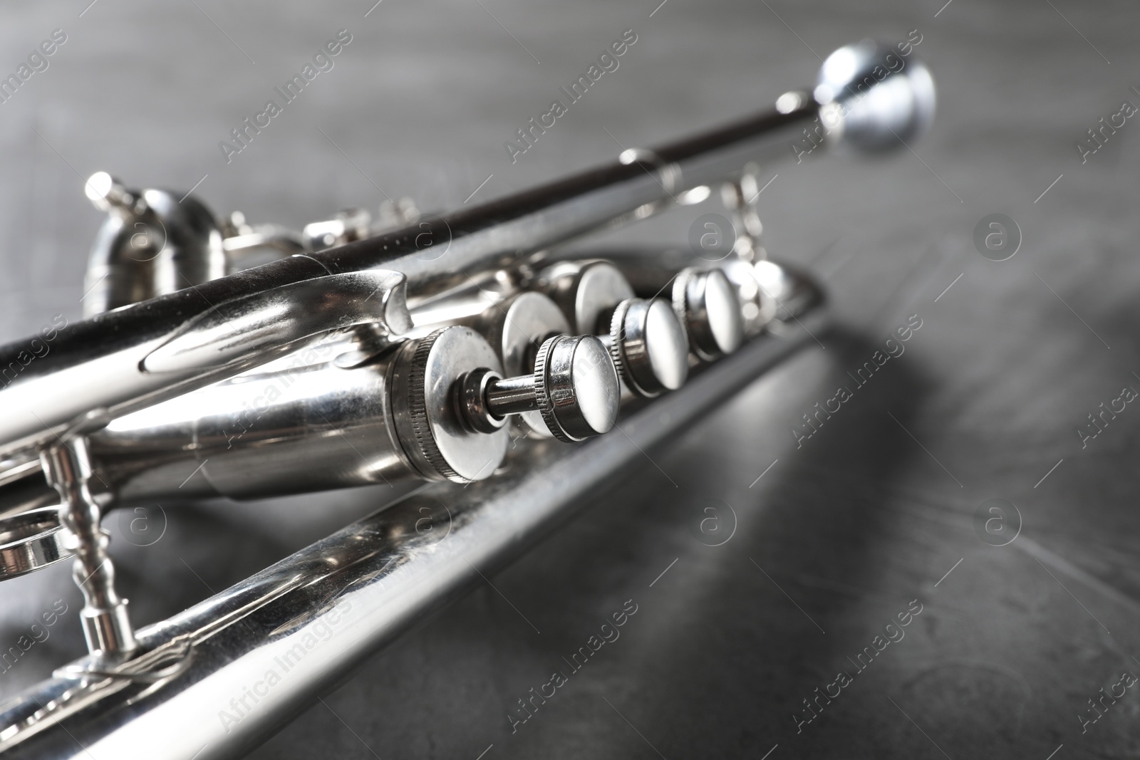 Photo of Closeup view of shiny trumpet on grey textured table. Wind musical instrument