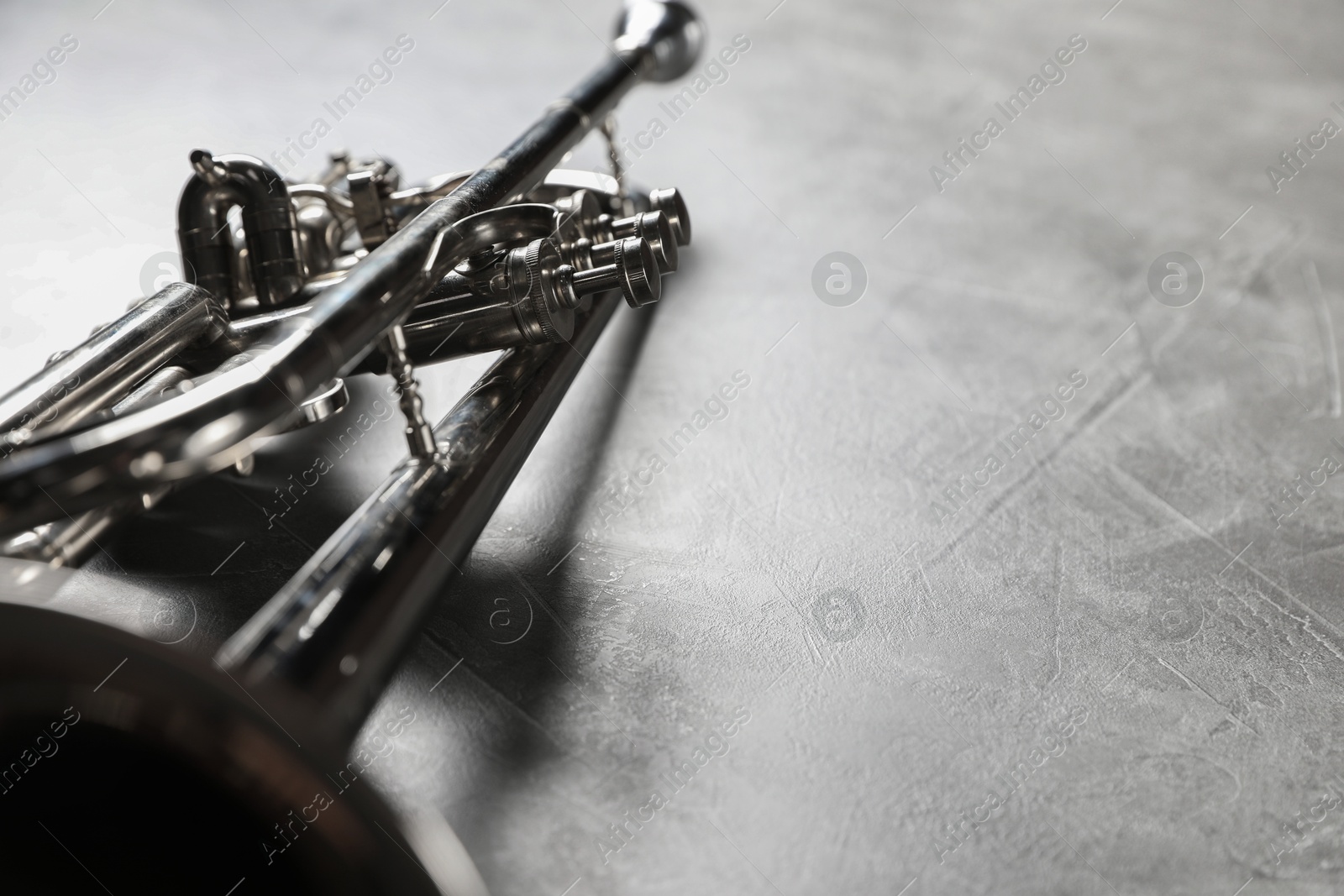 Photo of Closeup view of shiny trumpet on grey textured table, space for text. Wind musical instrument