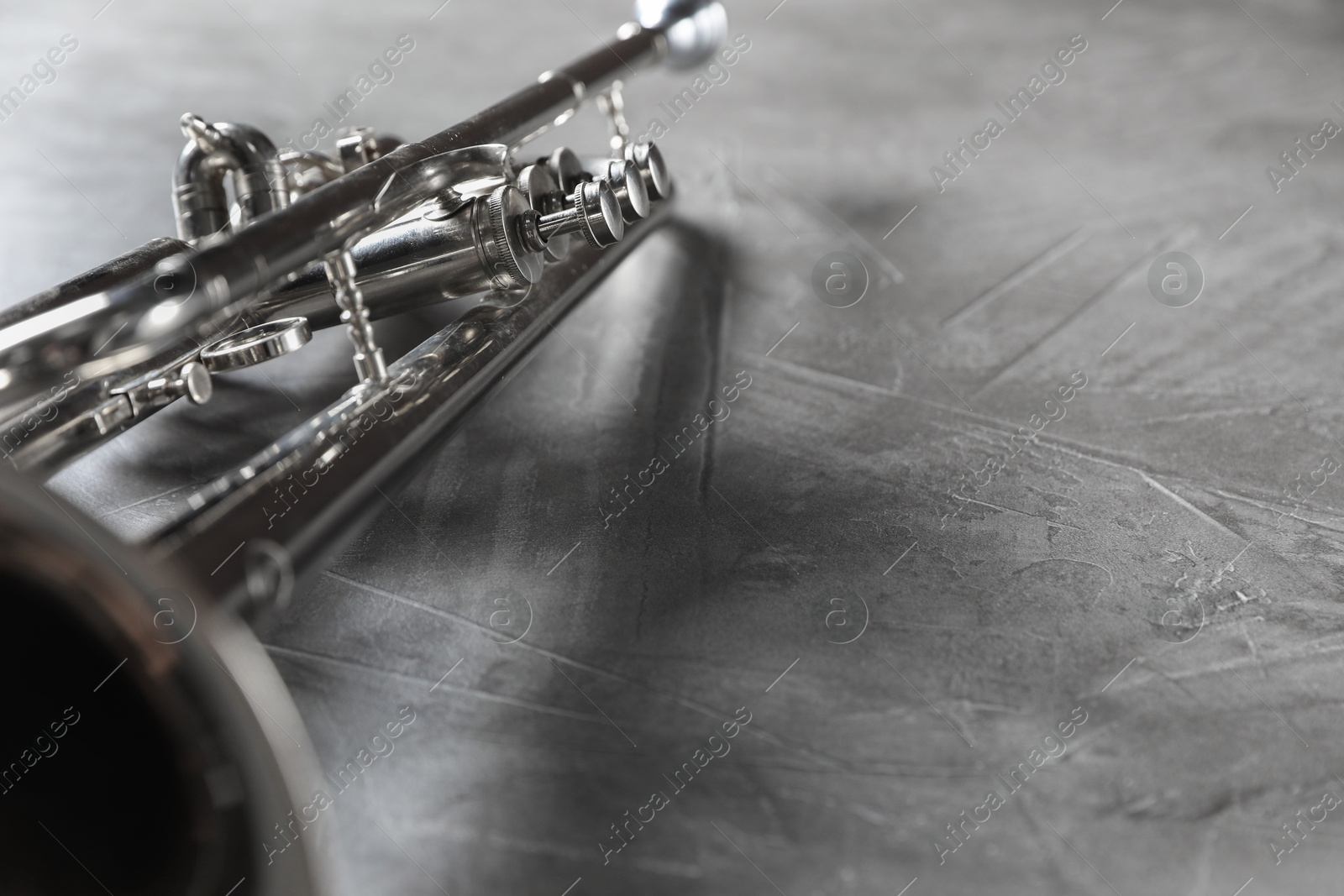 Photo of Closeup view of shiny trumpet on grey textured table, space for text. Wind musical instrument