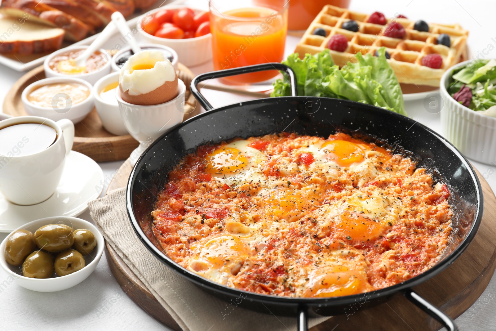 Photo of Tasty shakshouka in frying pan and other meals served for breakfast on white table, closeup