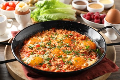 Photo of Tasty shakshouka in frying pan served for breakfast on wooden table, closeup