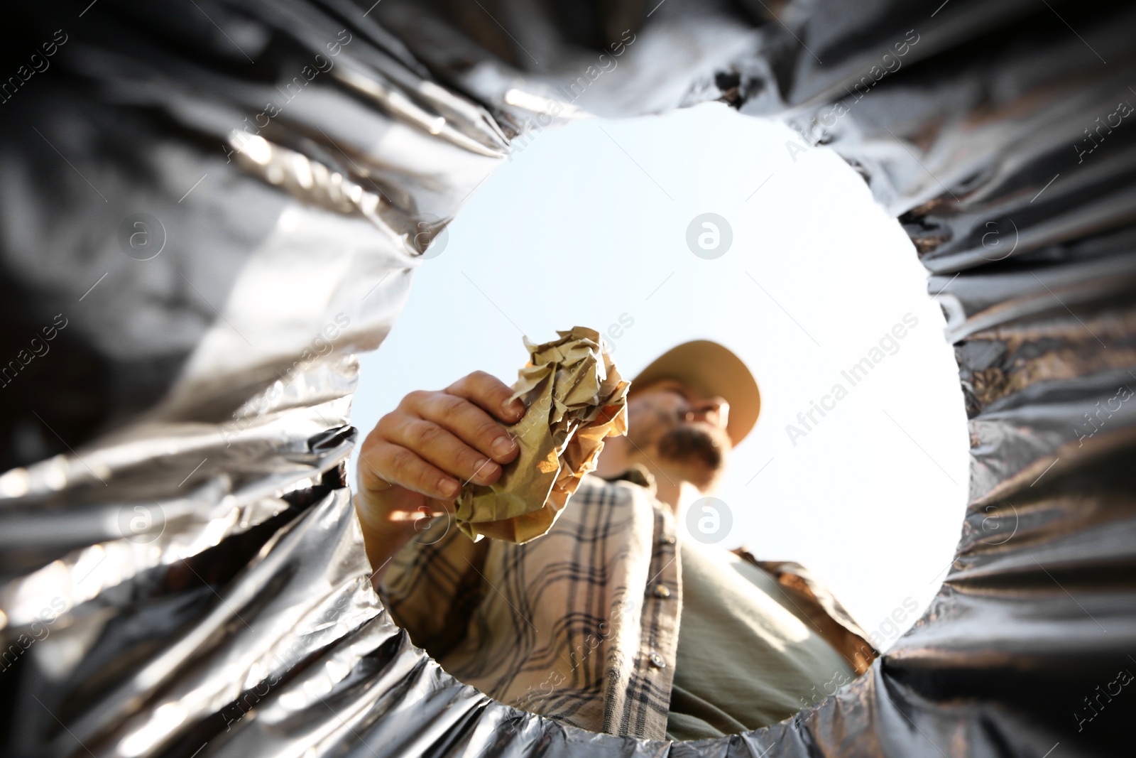 Photo of Man throwing garbage into trash bin outdoors, bottom view