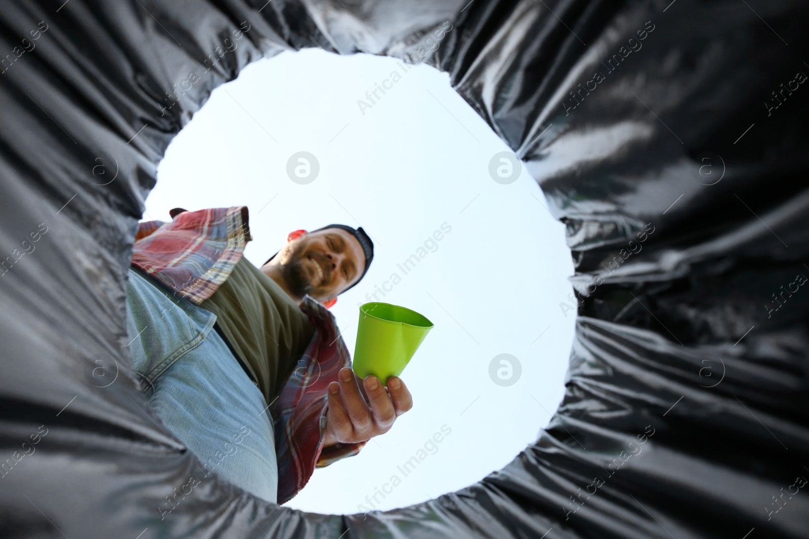 Photo of Man throwing garbage into trash bin outdoors, bottom view