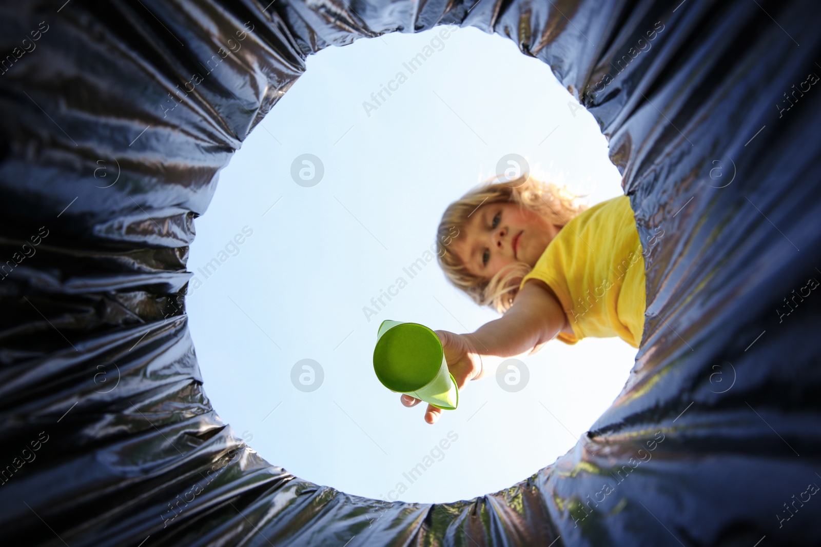 Photo of Cute little girl throwing garbage into trash bin outdoors, bottom view