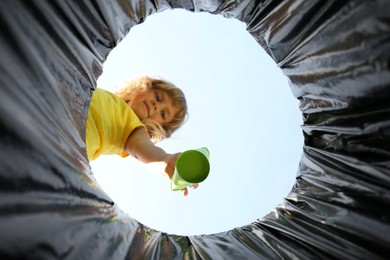 Cute little girl throwing garbage into trash bin outdoors, bottom view