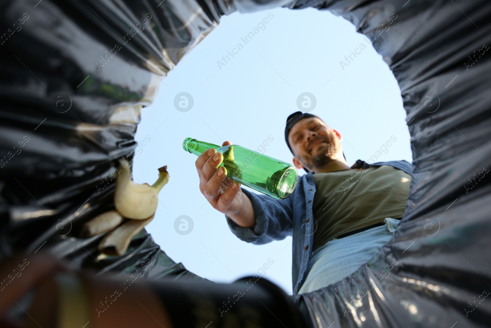 Photo of Man throwing glass bottle into garbage bin outdoors, bottom view