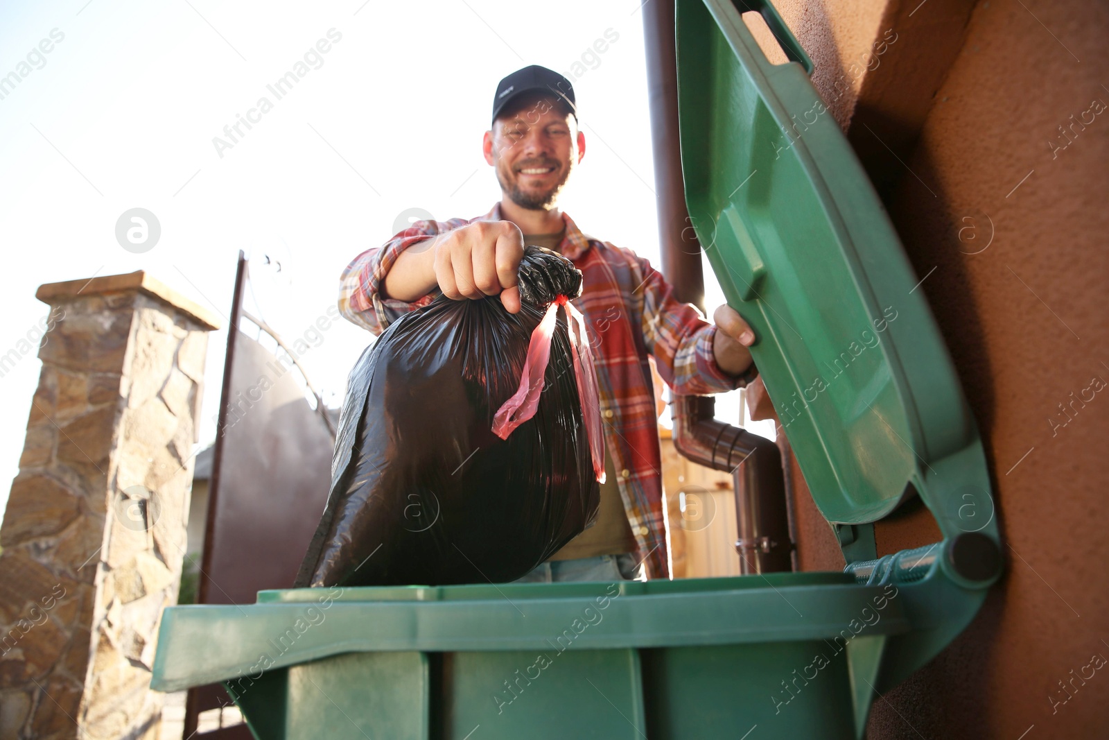 Photo of Man throwing trash bag full of garbage into bin outdoors, low angle view