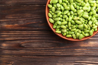 Photo of Raw green edamame soybeans in bowl on wooden table, top view. Space for text