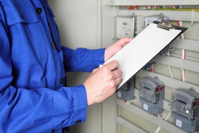 Technician worker with clipboard inspecting electricity meter, closeup