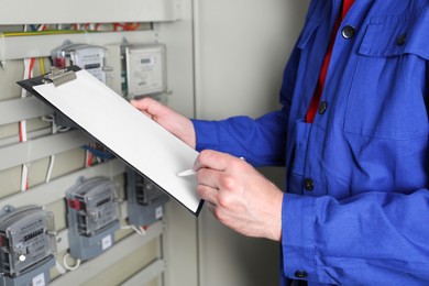 Photo of Technician worker with clipboard inspecting electricity meter, closeup